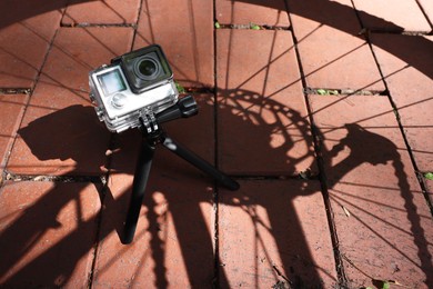 Photo of Modern action camera with tripod on pavement outdoors, above view. Space for text