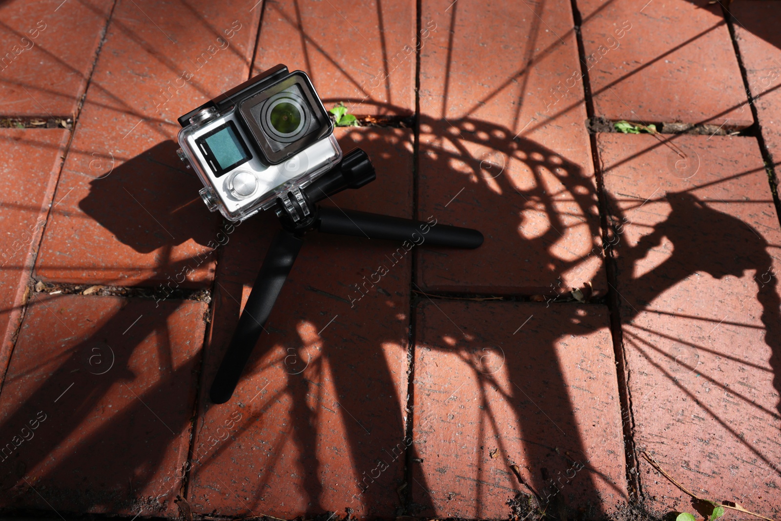 Photo of Modern action camera with tripod on pavement outdoors, above view. Space for text