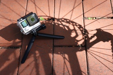 Photo of Modern action camera with tripod on pavement outdoors, above view. Space for text