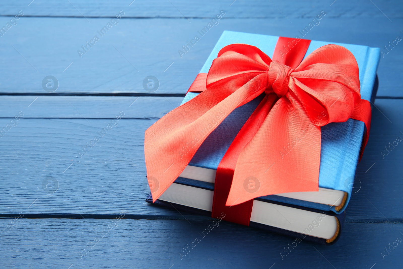 Photo of Books tied with red ribbon on blue wooden table, closeup. Space for text