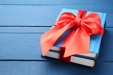 Books tied with red ribbon on blue wooden table, closeup. Space for text