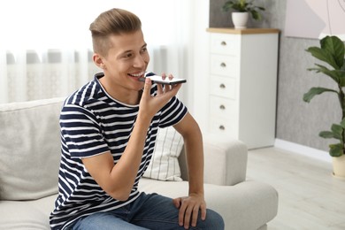 Photo of Young man recording voice message via smartphone at home