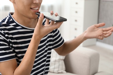 Young man recording voice message via smartphone at home, closeup