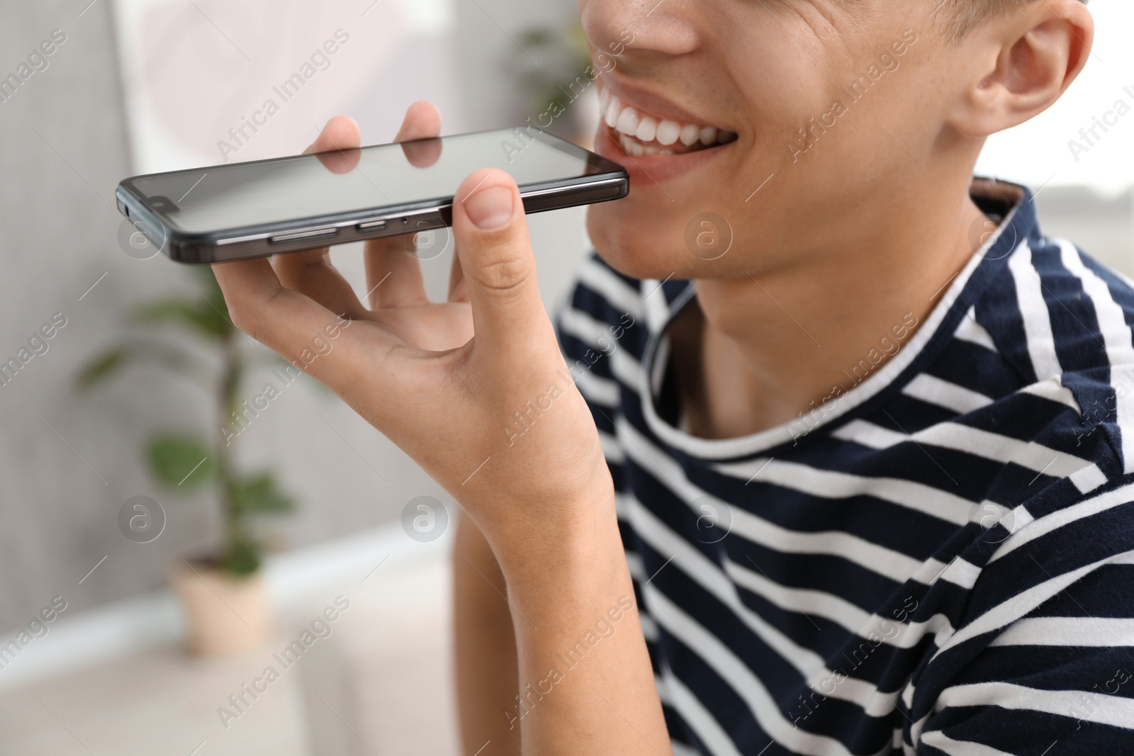 Photo of Young man recording voice message via smartphone at home, closeup