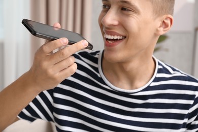 Photo of Young man recording voice message via smartphone at home, selective focus