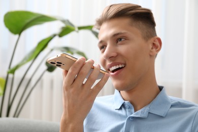 Young man recording voice message via smartphone at home, selective focus