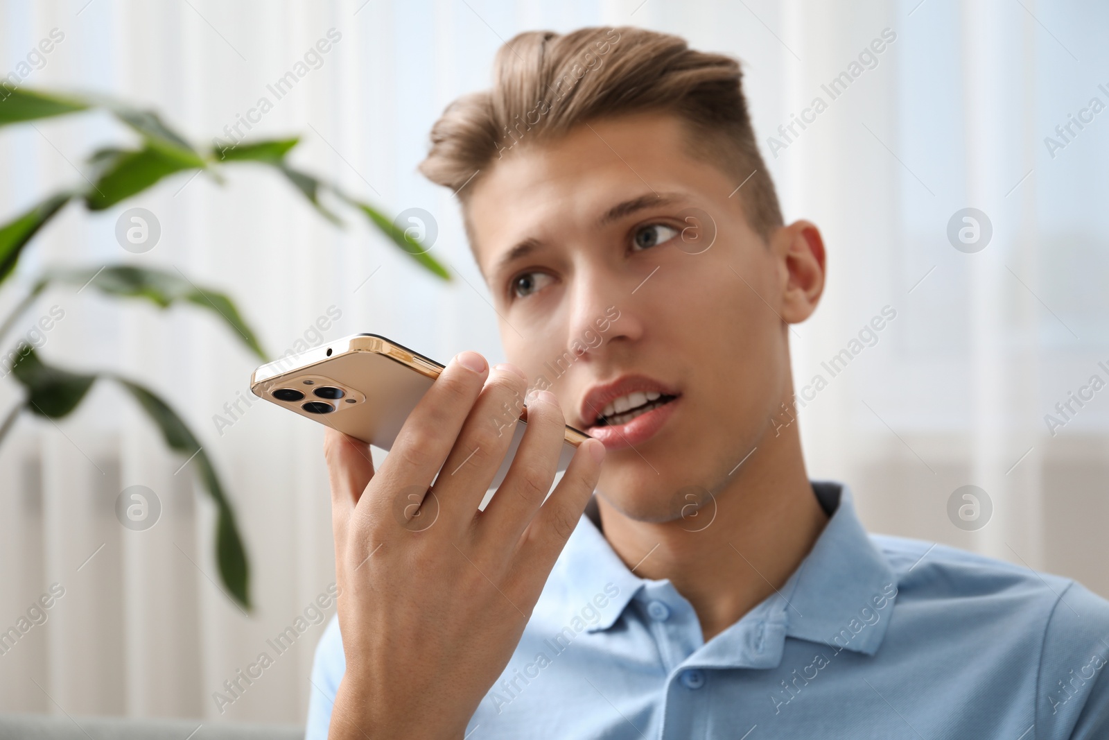 Photo of Young man recording voice message via smartphone at home