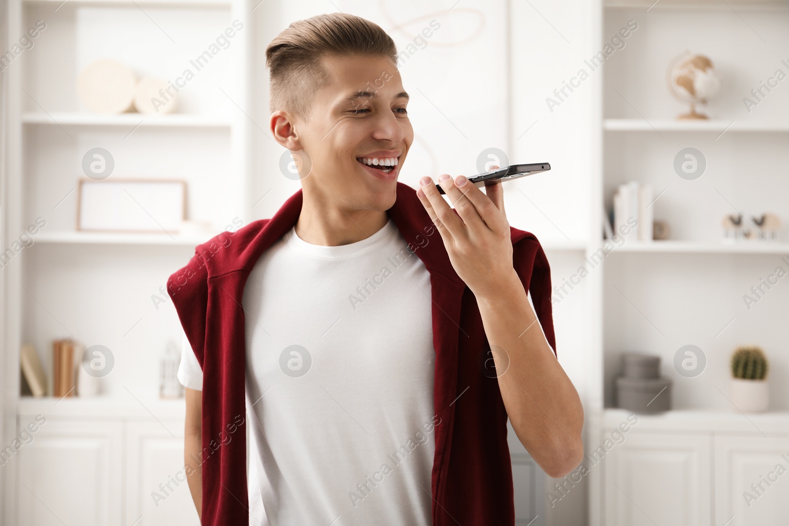 Photo of Young man recording voice message via smartphone at home