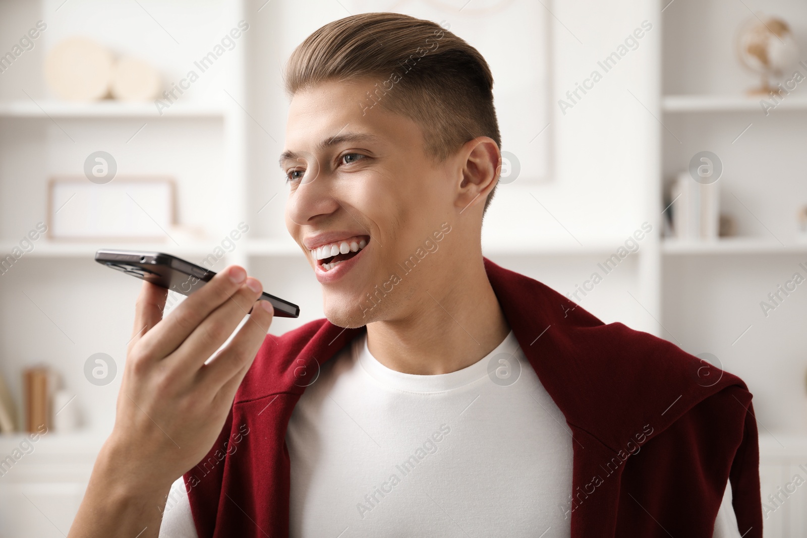 Photo of Young man recording voice message via smartphone at home