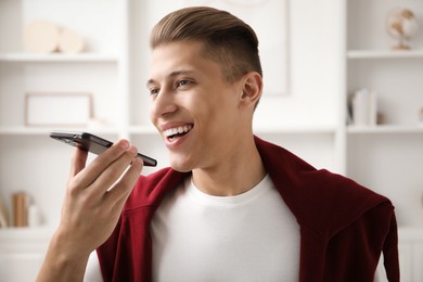 Photo of Young man recording voice message via smartphone at home