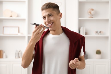 Young man recording voice message via smartphone at home