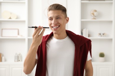 Photo of Young man with smartphone listening to voice message at home