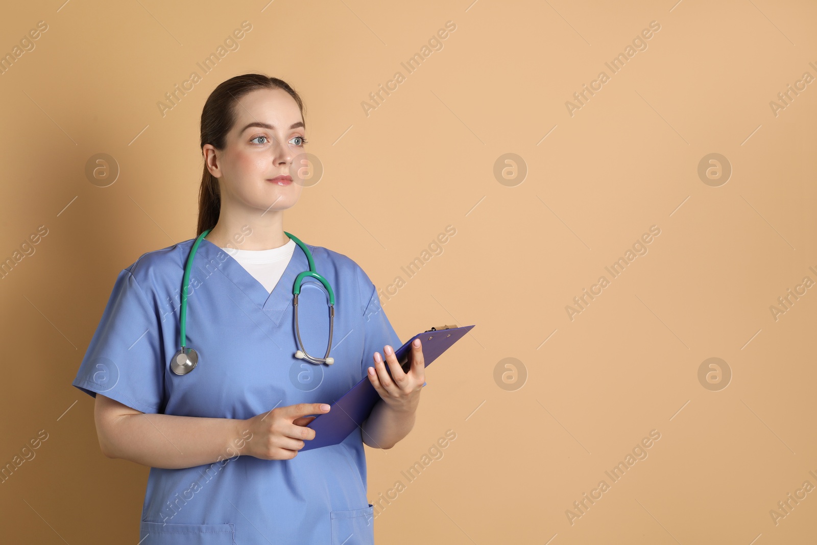 Photo of Portrait of professional nurse with stethoscope and clipboard on dark beige background