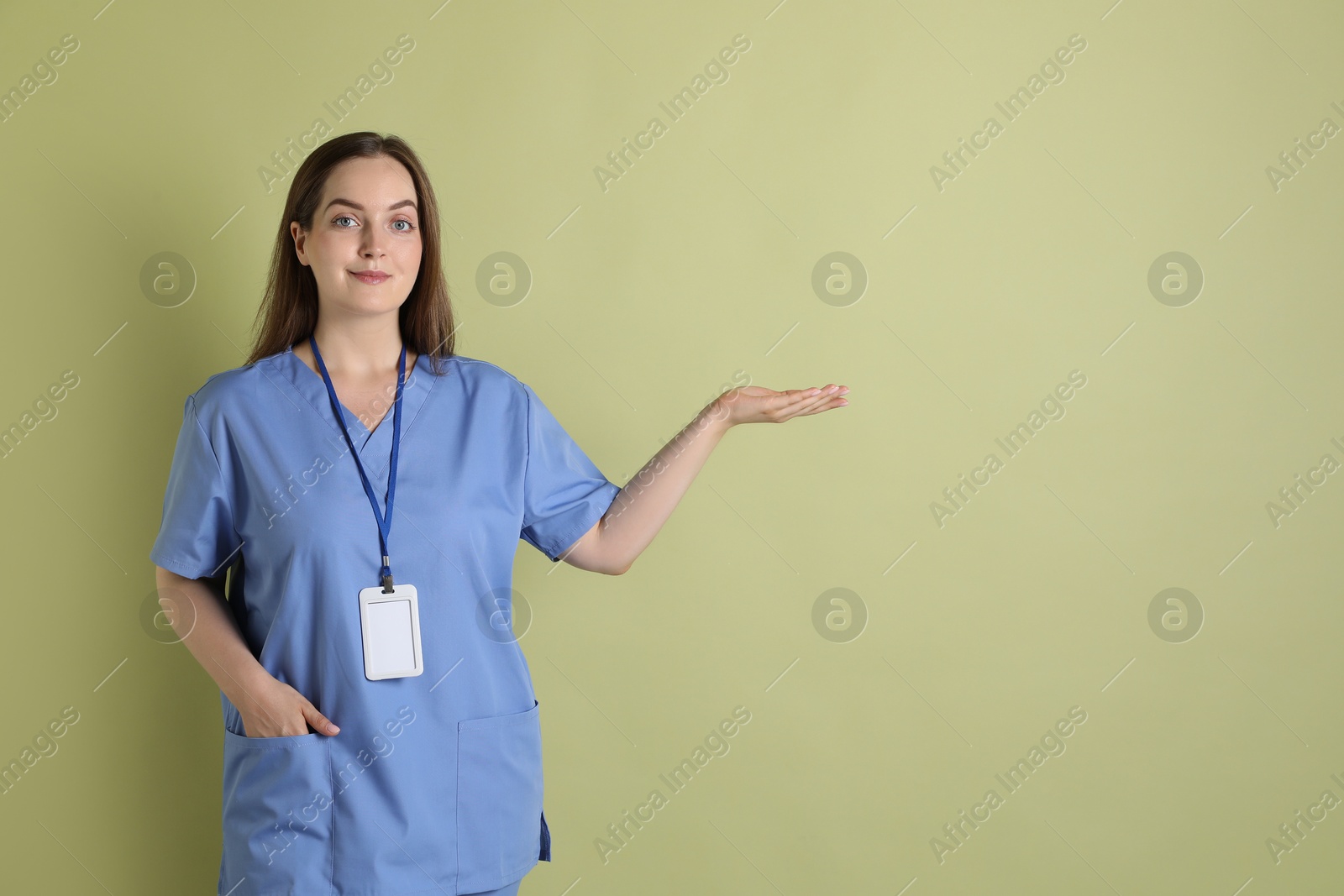 Photo of Professional nurse with badge pointing at something on pale green background. Space for text