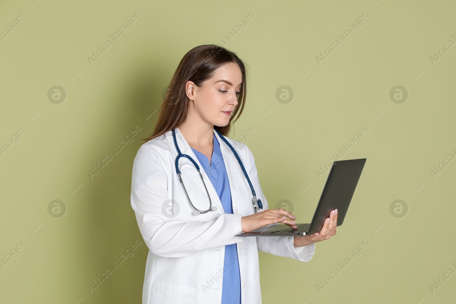 Photo of Professional nurse working with laptop on pale green background