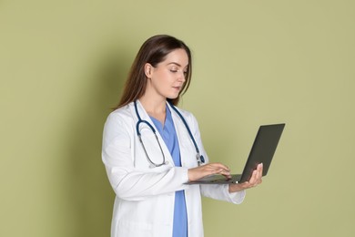 Photo of Professional nurse working with laptop on pale green background