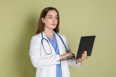 Photo of Professional nurse working with laptop on pale green background