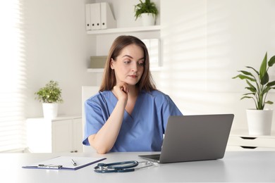 Photo of Young nurse working with laptop at desk in hospital