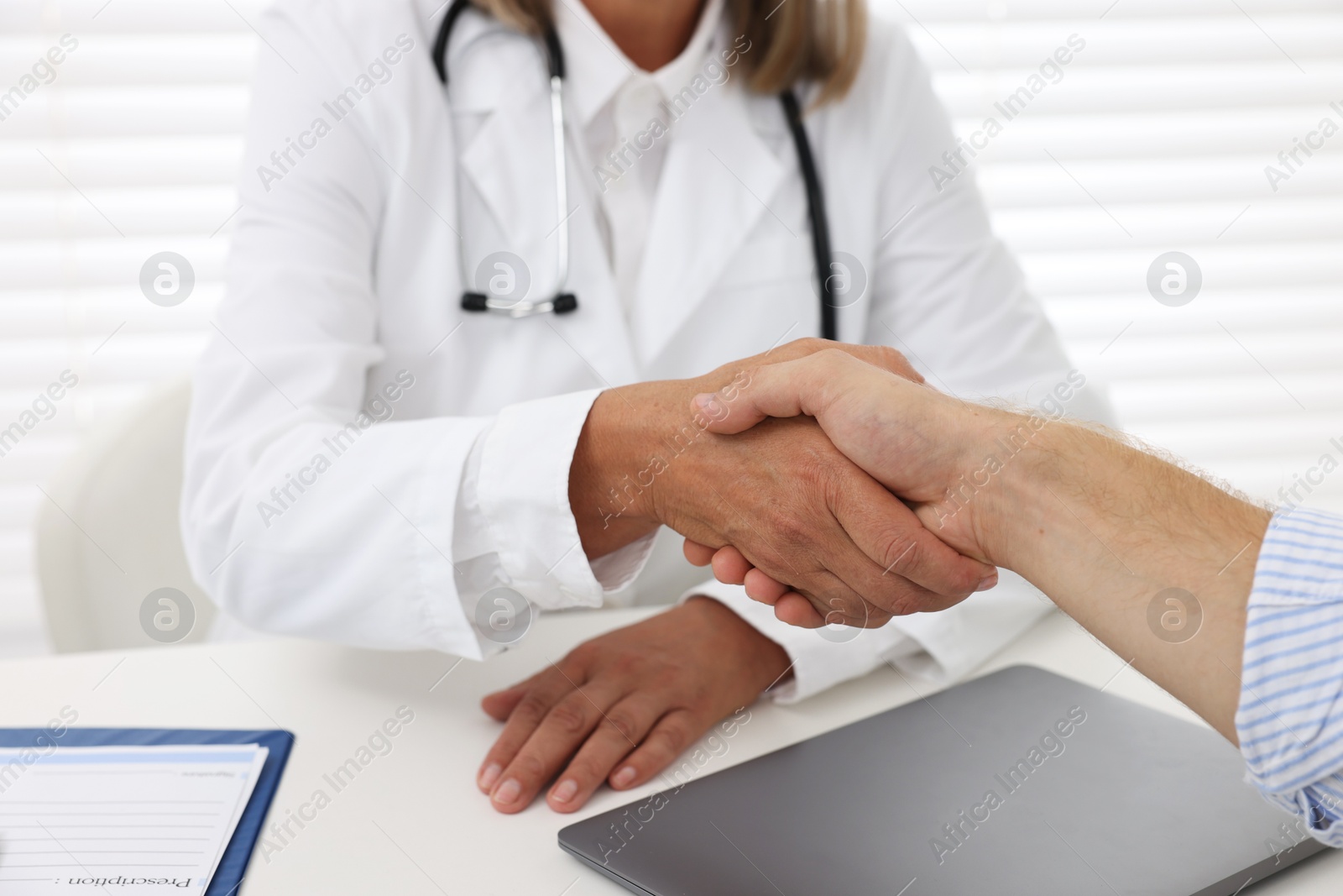 Photo of Senior doctor shaking hands with patient in hospital, closeup