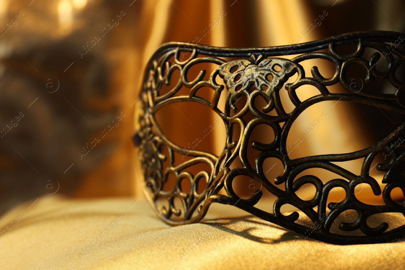 Photo of One beautiful carnival mask on golden fabric, closeup. Space for text