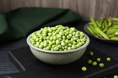 Photo of Fresh green peas in bowl on black wooden table, closeup