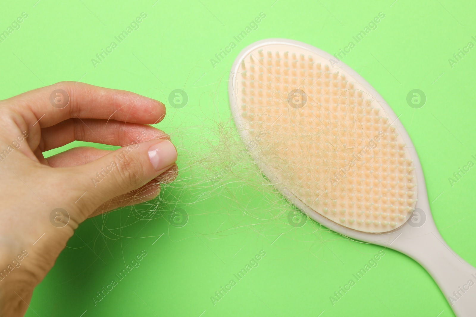 Photo of Woman taking her lost hair from brush on light green background, top view. Alopecia problem