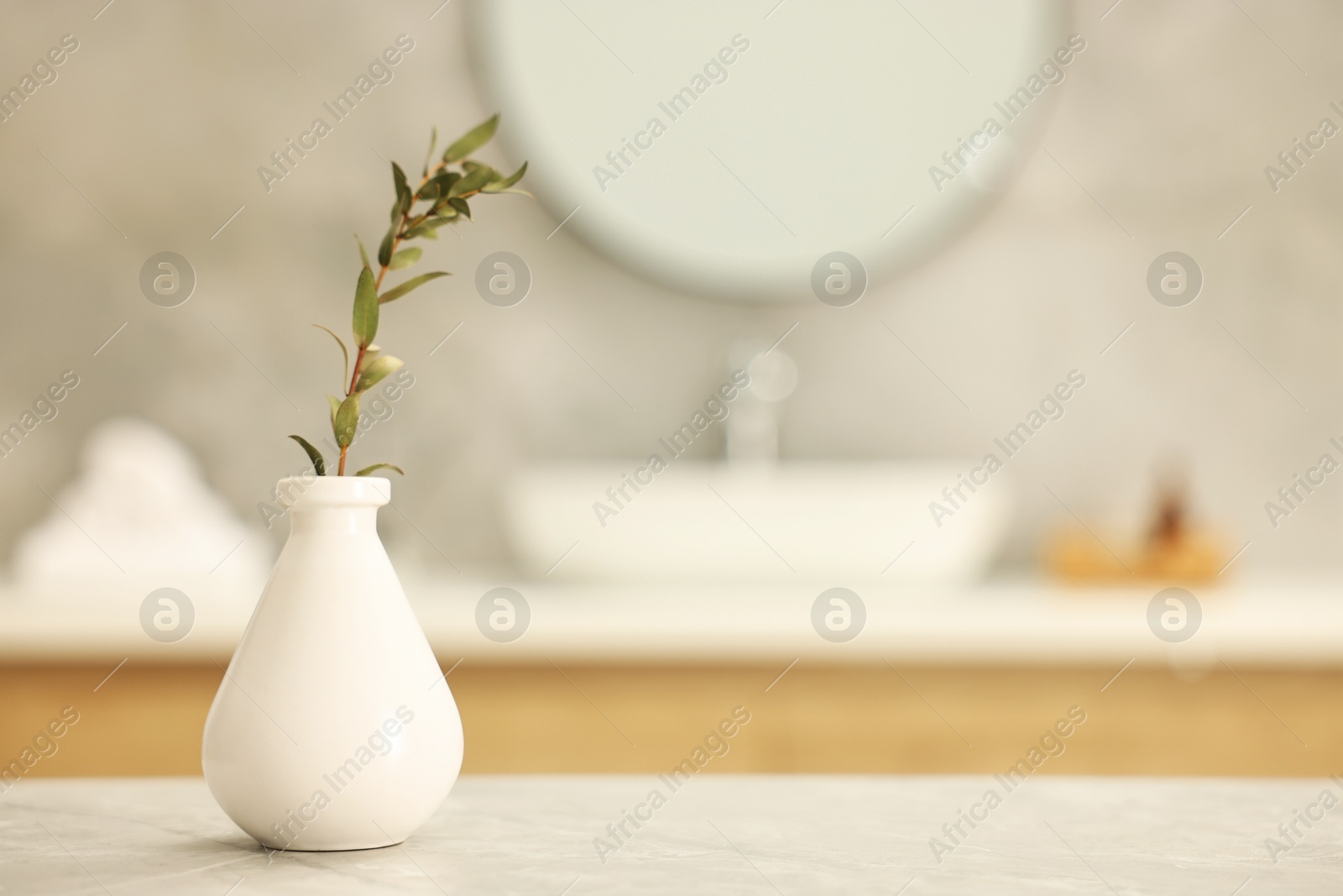 Photo of Vase with green twig on light grey table in bathroom, space for text