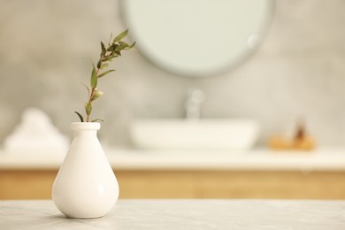 Vase with green twig on light grey table in bathroom, space for text