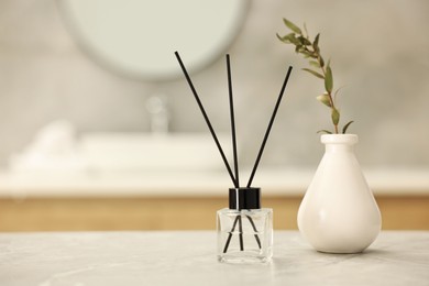 Reed diffuser and vase with green twig on light grey marble table in bathroom, space for text