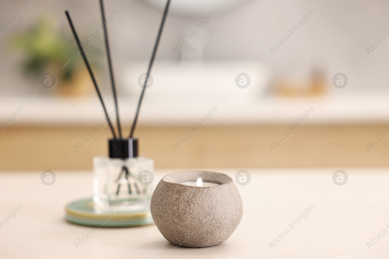 Photo of Burning candle and reed diffuser on light table in bathroom