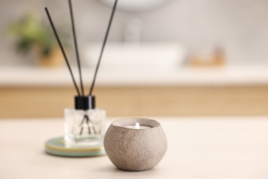 Burning candle and reed diffuser on light table in bathroom