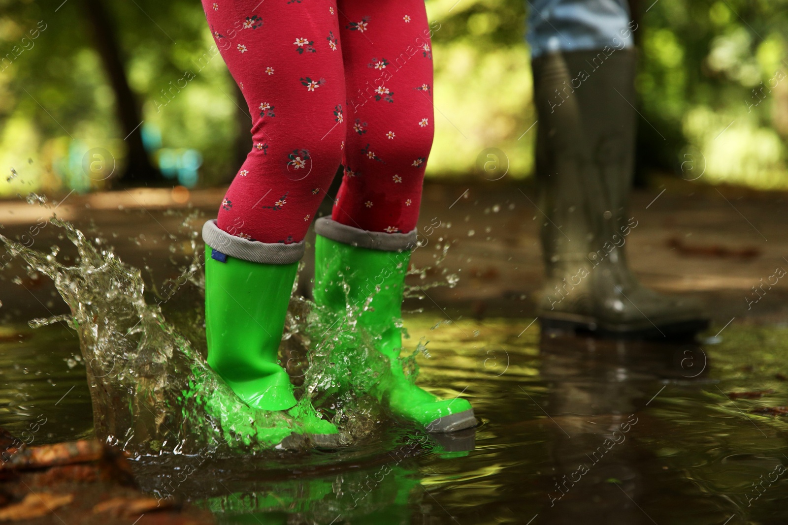 Photo of Mother and daughter wearing rubber boots standing in puddle outdoors, closeup