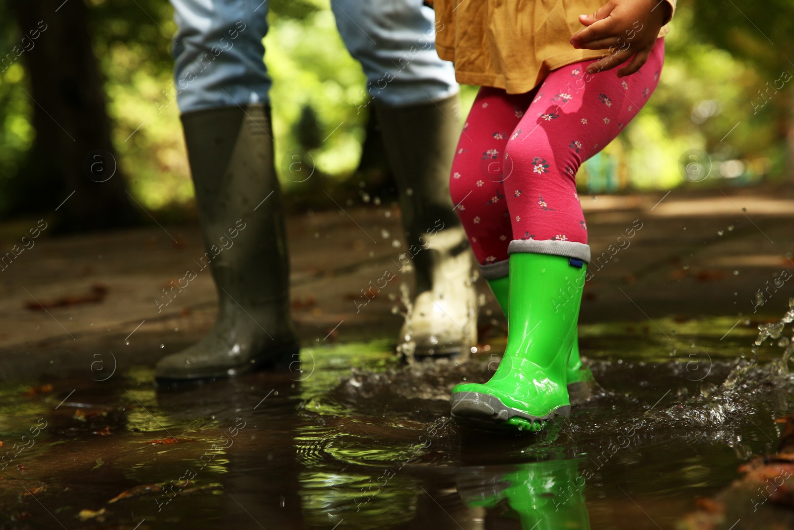 Photo of Mother and daughter wearing rubber boots walking in puddle outdoors, closeup