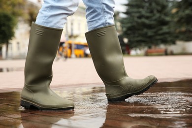 Woman wearing rubber boots walking in puddle outdoors, closeup