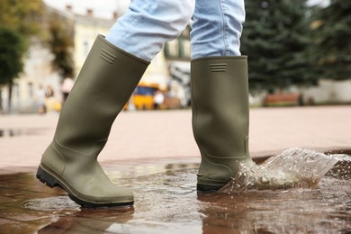 Photo of Woman wearing rubber boots walking in puddle outdoors, closeup