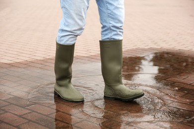 Photo of Woman wearing rubber boots walking in puddle outdoors, closeup