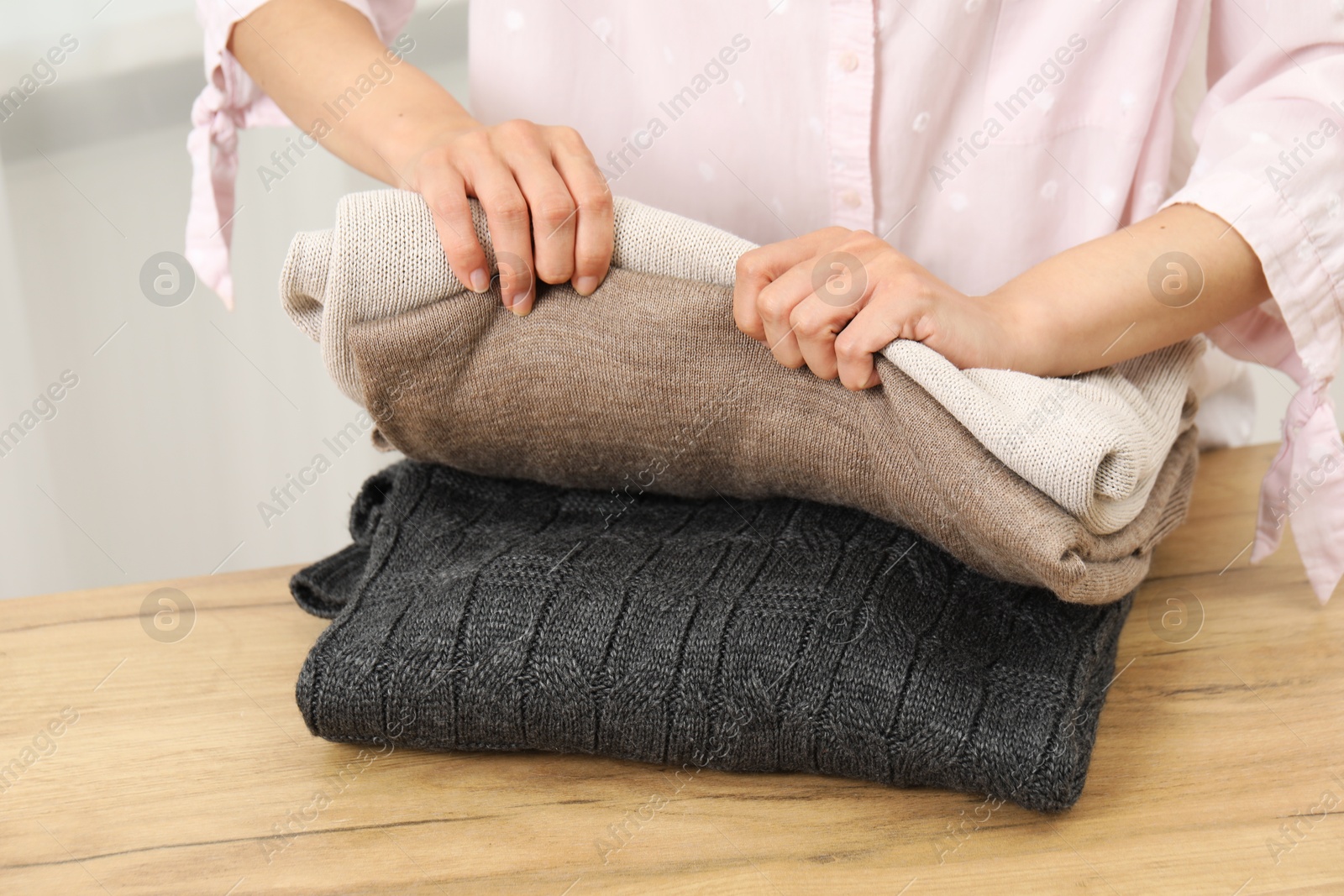 Photo of Woman folding clothes at wooden table indoors, closeup