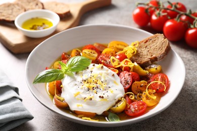 Photo of Delicious fresh burrata salad in bowl on gray textured table, closeup