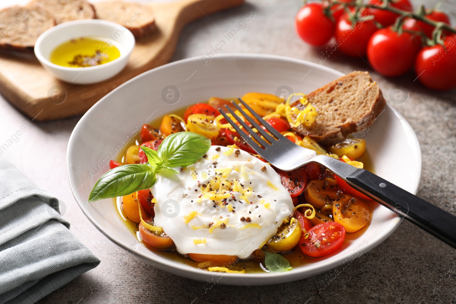 Photo of Delicious fresh burrata salad in bowl served on gray textured table, closeup