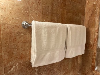 Soft terry towels hanging on tiled wall in hotel bathroom