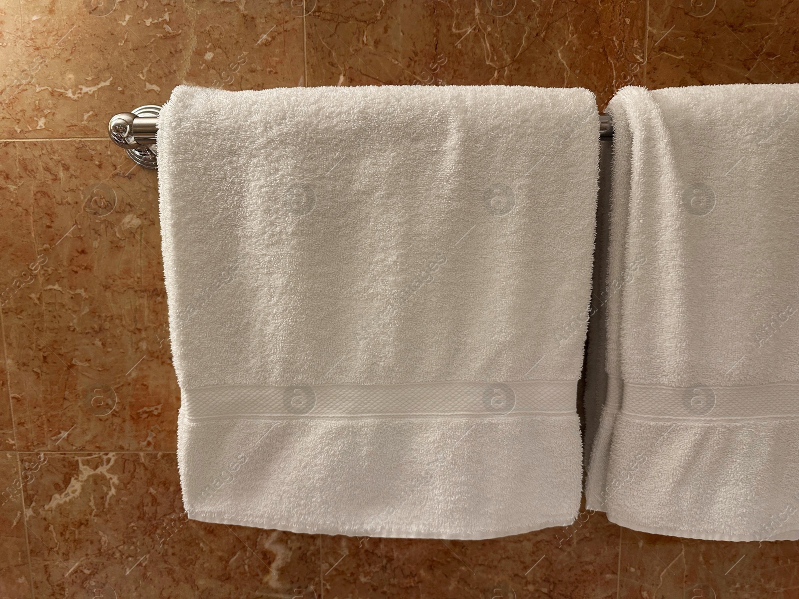 Photo of Soft terry towels hanging on tiled wall in hotel bathroom