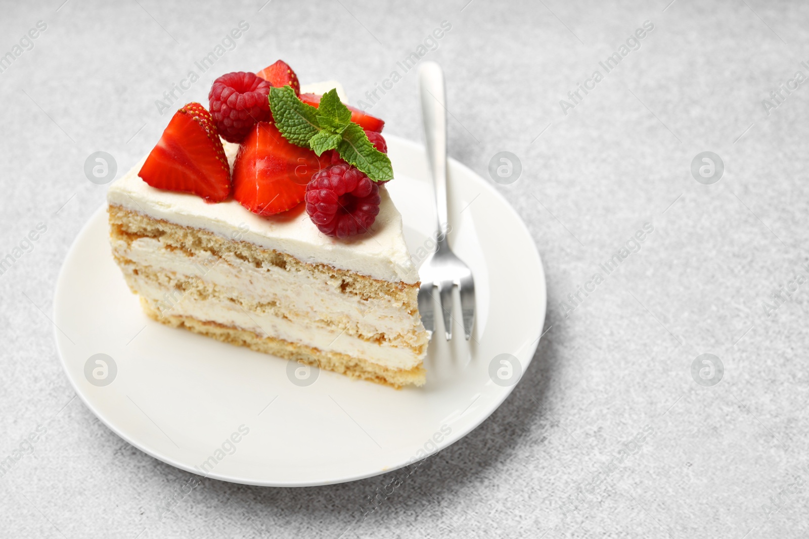 Photo of Piece of tasty sponge cake with fresh berries and mint served on light gray table, space for text