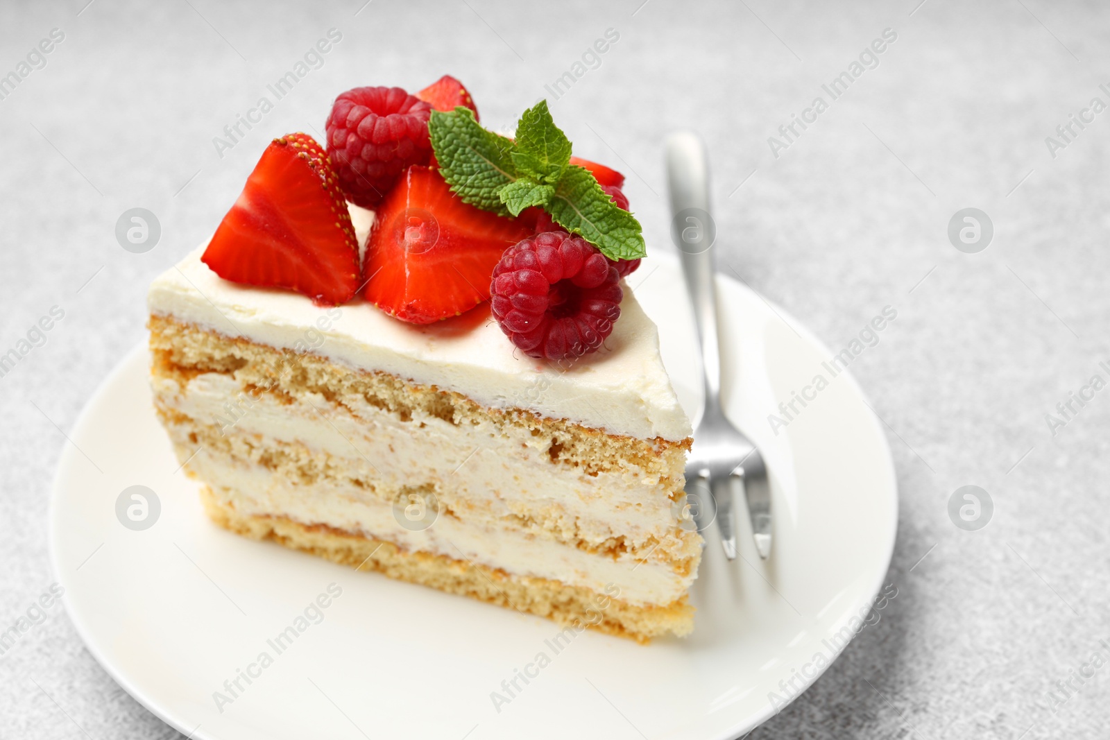 Photo of Piece of tasty sponge cake with fresh berries and mint served on light gray table, closeup