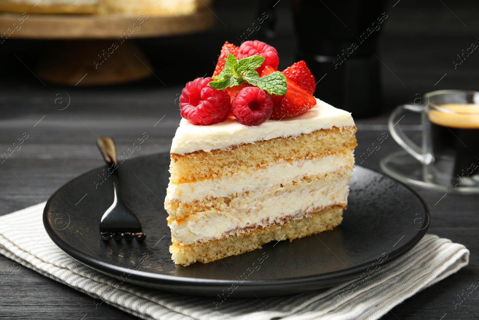 Photo of Piece of tasty sponge cake with fresh berries and mint served on black wooden table, closeup