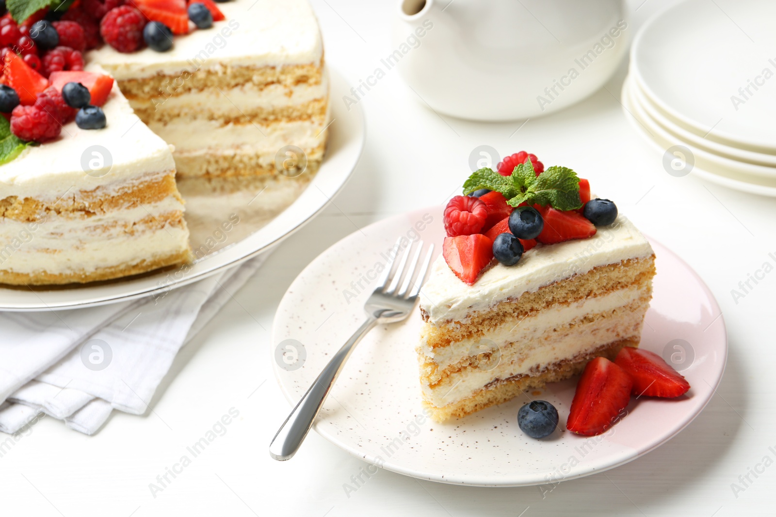 Photo of Tasty sponge cake with fresh berries and mint served on white table