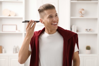 Young man with smartphone listening to voice message at home