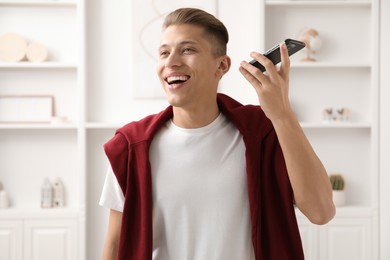 Young man with smartphone listening to voice message at home