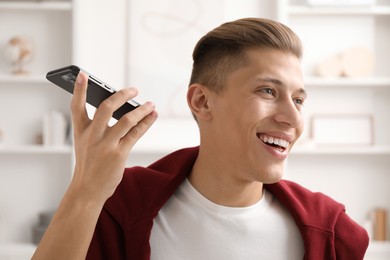 Photo of Young man with smartphone listening to voice message at home