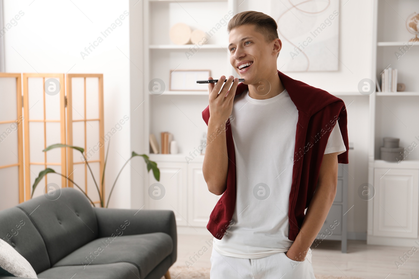 Photo of Young man recording voice message via smartphone at home