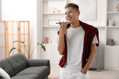 Photo of Young man recording voice message via smartphone at home